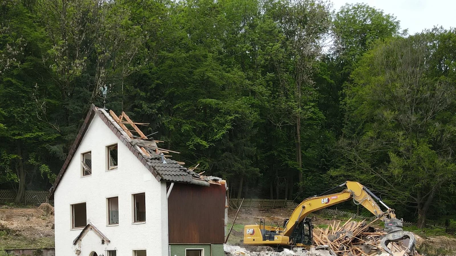 Referenzprojekt Hausabriss: Wohnhaus mit bereits zurückgebautem Dach, daneben Kettenbagger mit Sortiergreifer